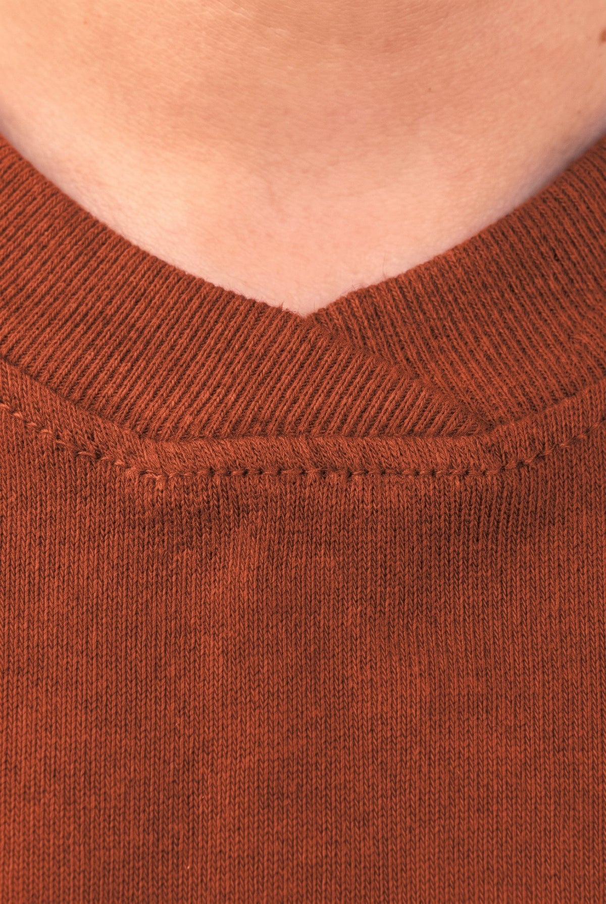Close-up of the ribbed V-neck collar with stitched tab on the brown tee